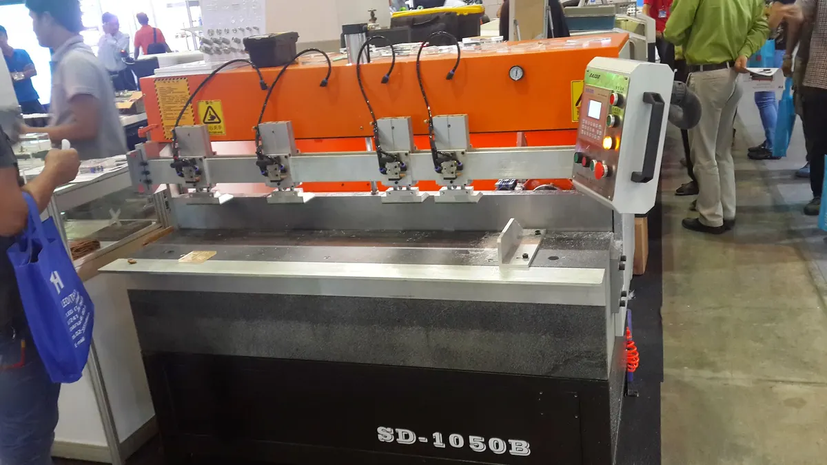 เครื่องจักรดัดพับสีส้มและเทา SD-1050B พร้อมแผงควบคุม ตั้งแสดงอยู่ในงานนิทรรศการ