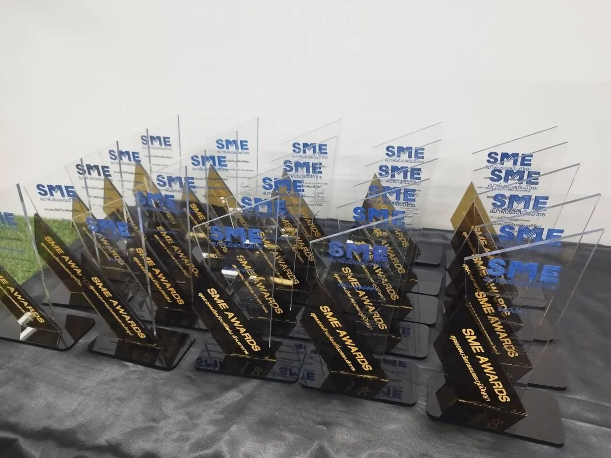 ถ้วยรางวัลอะคริลิคใสรูปทรงสามเหลี่ยม สกรีนโลโก้ SME AWARDS จัดวางเรียงกันหลายชิ้นบนโต๊ะ