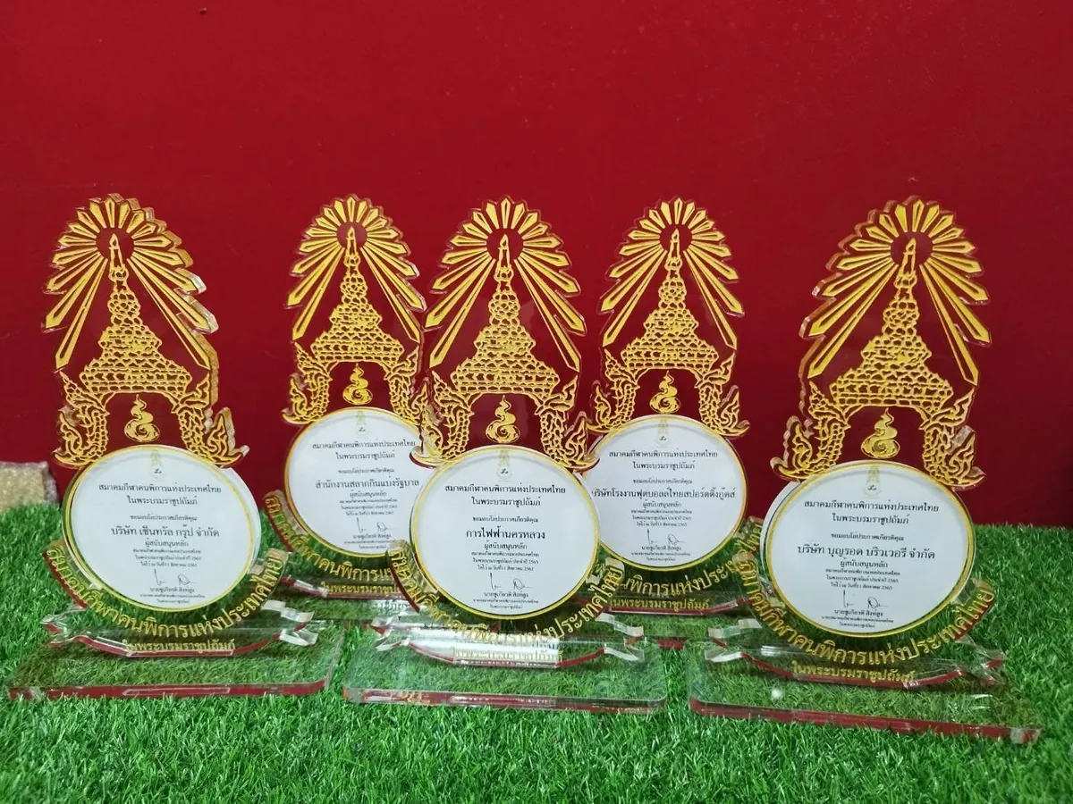 โล่รางวัลอะคริลิคใสสลักลายไทยสีทองพร้อมข้อความภาษาไทยวางเรียงกันห้าชิ้นบนพื้นหญ้าเทียม